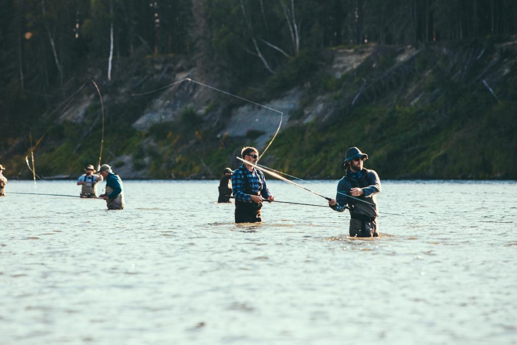 A group of men standing waist deep in a river, casting their fishing lines.